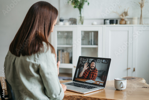 Video call, video meeting. A young woman is discussing some business tasks with a young man via video, she sits at office space and looks at webcam