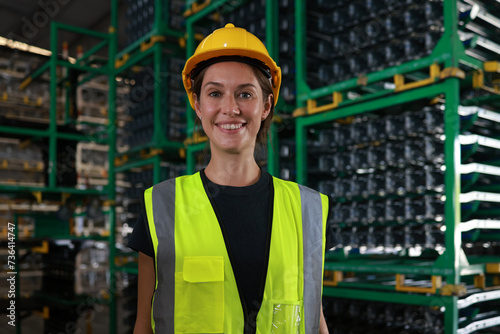 At the raw material storage in the warehouse distribution, there is a portrait of a young woman wearing a green safety reflector vest, who is ready to supply materials to the production line. photo