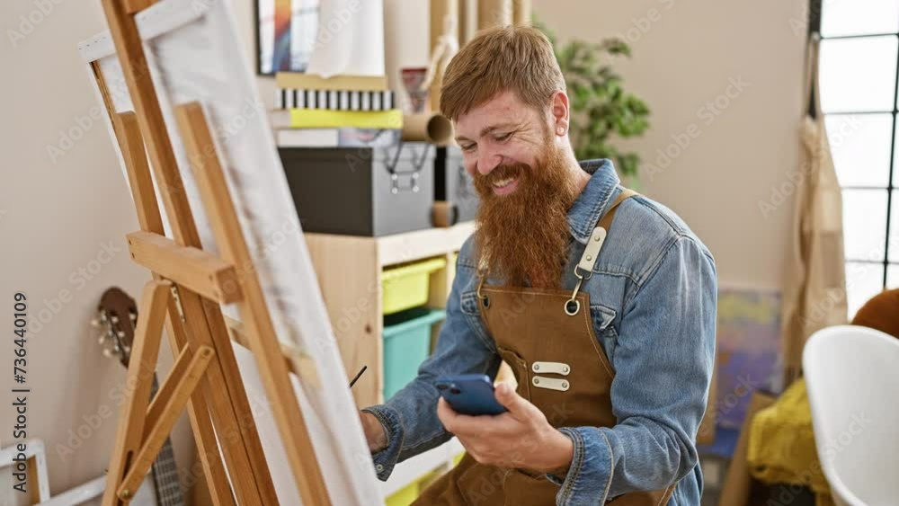 Confident redhead young man, a smiling artist, carefully drawing on smartphone in art studio classroom