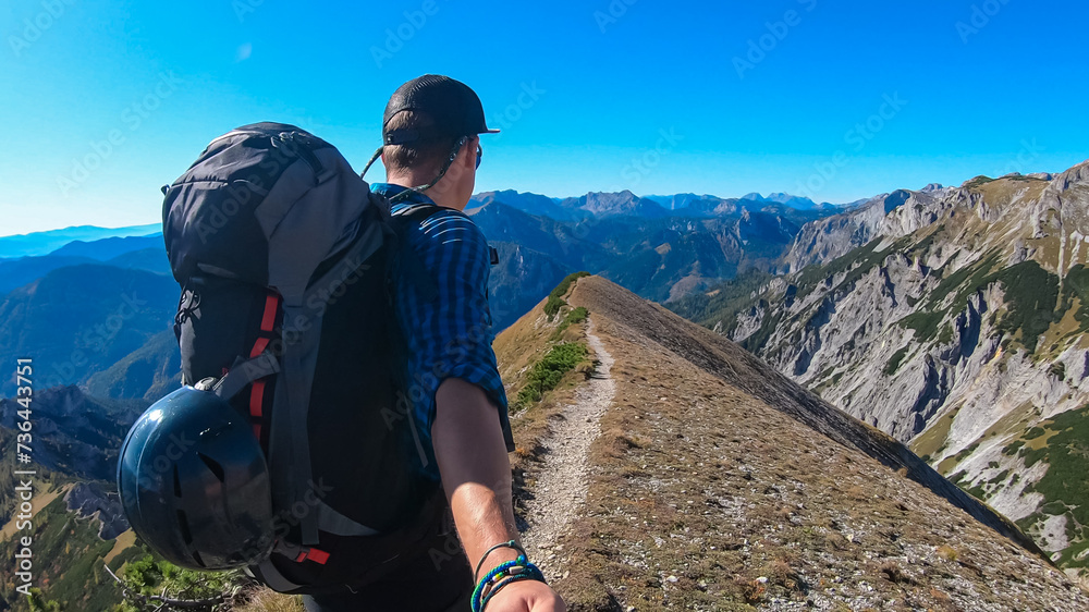 Hiker man on idyllic hiking trail on alpine meadow with scenic view of majestic Hochschwab mountain range, Styria, Austria. Wanderlust in remote Austrian Alps. Sense of escapism, peace, reflection