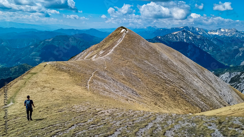 Hiker man on idyllic hiking trail on alpine meadow with scenic view of majestic Hochschwab mountain range  Styria  Austria. Wanderlust in remote Austrian Alps. Sense of escapism  peace  reflection