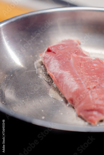 close-up of a piece of pink duck breast on hot frying pan, beginning to fry