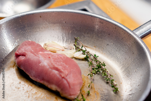 close-up of a piece of pink duck breast with rosemary on hot frying pan starting to fry photo