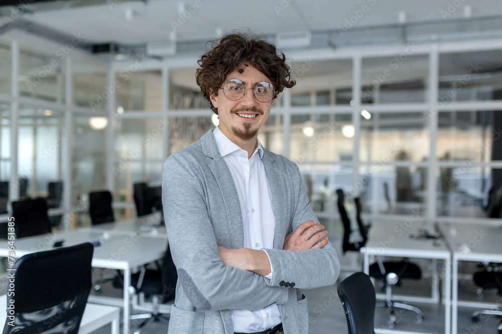 Portrait of a young mature male professional with curly hair confidently standing in a well-lit corporate office. Portrait of a young mature male professional with curly hair confidently standing in a well-lit corporate office.