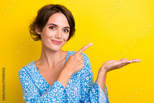 Portrait of lovely gorgeous cheerful girl wear blue blouse indicating at object on palm empty space isolated on yellow color background