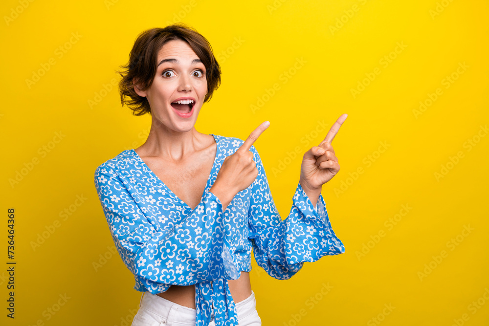 Photo of adorable excited young woman wear print blouse open mouth pointing two fingers empty space isolated yellow color background Photo of adorable excited young woman wear print blouse open mouth pointing two fingers empty space isolated yellow color background