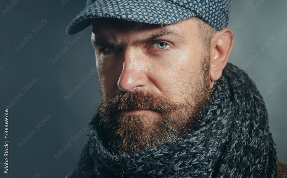 Closeup portrait of serious man with beard in cap and scarf. Winter accessories. Handsome bearded man in gray scarf and hat. Attractive male in fashionable clothing. Autumn-winter fashion for men. Closeup portrait of serious man with beard in cap and scarf. Winter accessories. Handsome bearded man in gray scarf and hat. Attractive male in fashionable clothing. Autumn-winter fashion for men.