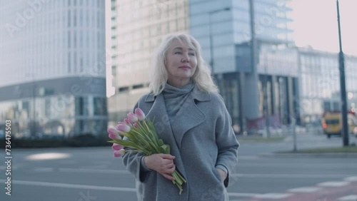 A senior woman with flowers in a big city