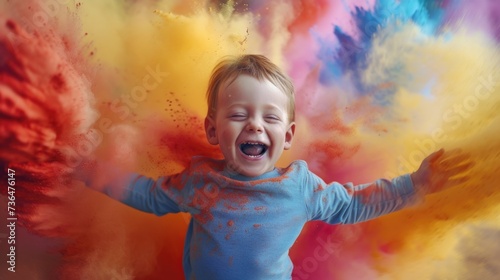 A young boy is seen with his arms stretched out wide and a huge smile on his face, exuding happiness and excitement. He is in the midst of a colorful explosion of fine powder, with hues of blue, pink,