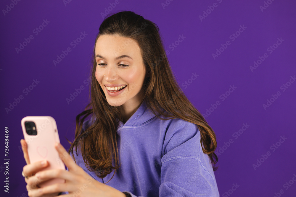 Great application or website. Portrait of excited woman using her mobile phone, isolated on purple studio background, copy space. Positive lady holding gadget, looking at phone, texting, messaging. Great application or website. Portrait of excited woman using her mobile phone, isolated on purple studio background, copy space. Positive lady holding gadget, looking at phone, texting, messaging.