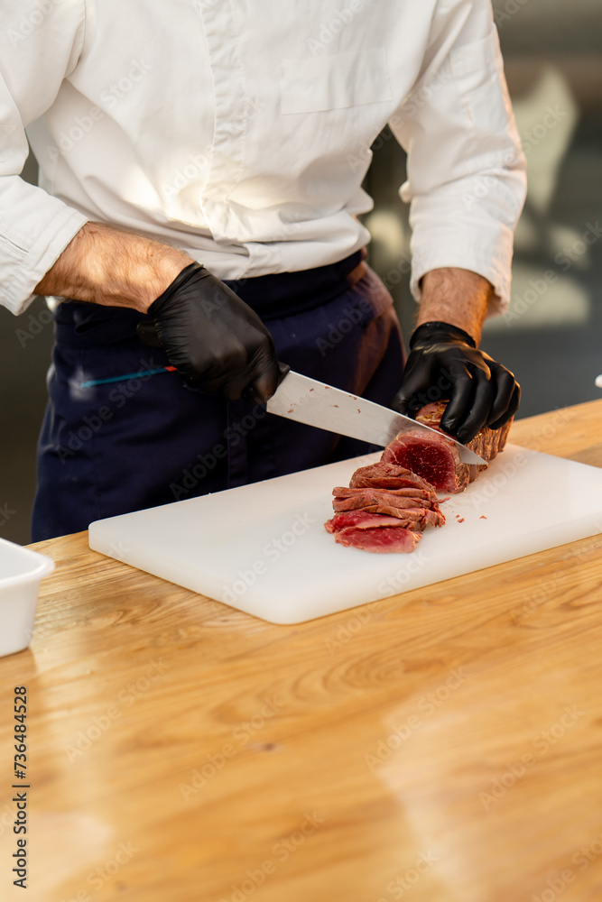 close-up of a chef's hands in black gloves cutting piece of raw jerky meat on a board