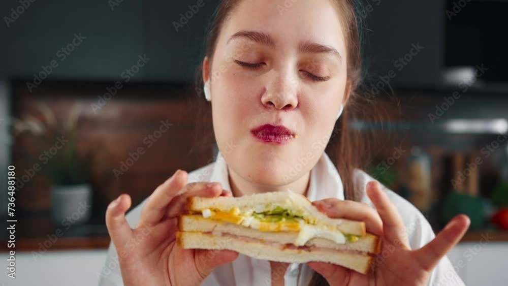 Woman eating fast food sandwich. Hungry girl eating fast food unhealthy fresh tasty sandwich hamburger with desire listening music close up. Enjoying unhealthy eating - junk food bakery concept. Woman eating fast food sandwich. Hungry girl eating fast food unhealthy fresh tasty sandwich hamburger with desire listening music close up. Enjoying unhealthy eating - junk food bakery concept.