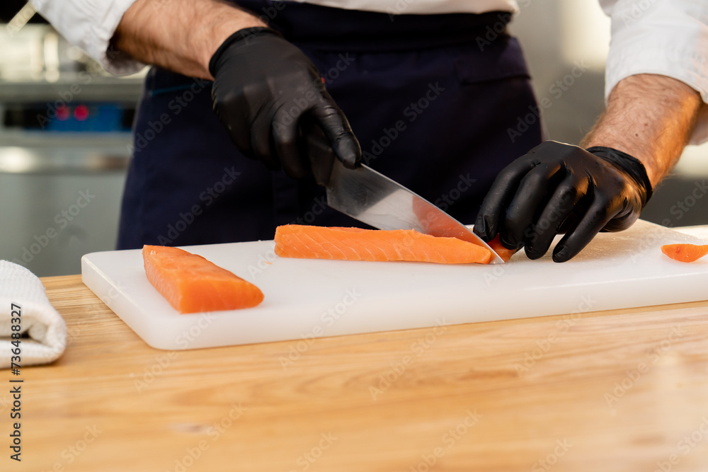 close-up of a chef's hands in black gloves cutting salmon fillet on white board