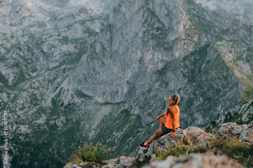 A sporty extreme runner is sitting on mountain cliff and enjoying scenery.