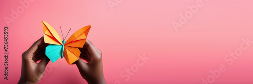 horizontal banner, Zero Discrimination Day, multicolored paper butterflies, rainbow coloring, origami butterfly in the hands of an African American woman, pink background, place for text photo