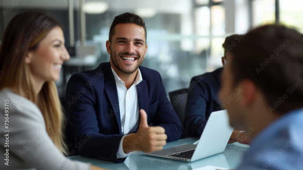 A confident professional man in a suit is giving a thumbs up in a bright office environment with cheerful colleagues around him, indicating success and approval.