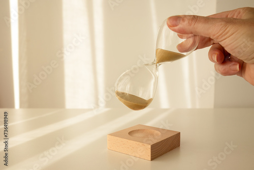 woman's hand holding time, depicted on an elegant glass hourglass with morning light background