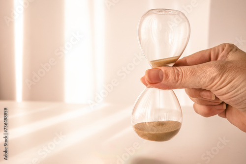 woman's hand holding time, depicted on an elegant glass hourglass with morning light background