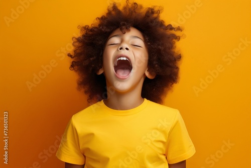 extremely whim Upset black curly haired boy in t shirt screaming and crying or very emotional expression sings songs with opened mouth and closed eyes against orange color wall photo