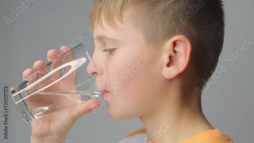 Cute boy drinks clean water from a glass on a gray background. portrait of a child with a glas photo