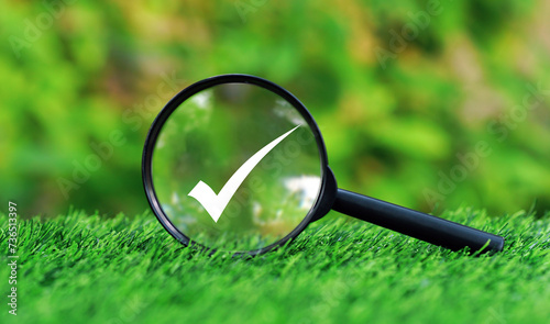 Magnifying glass focused on check mark on green grass in nature garden background, Check mark approved symbol on land in nature background.