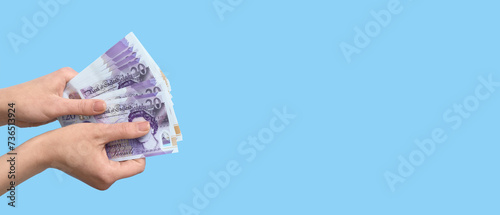 Female hands holding pound sterling banknotes on light blue background with space for text photo