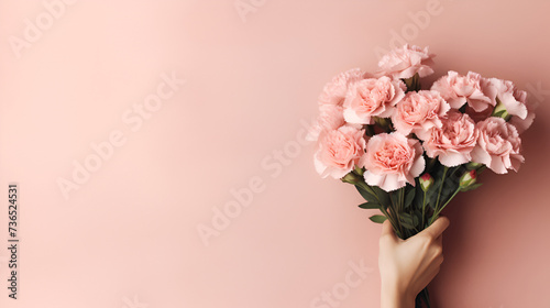 Female hands holding a bouquet of pink flowers close-up on a pink background.