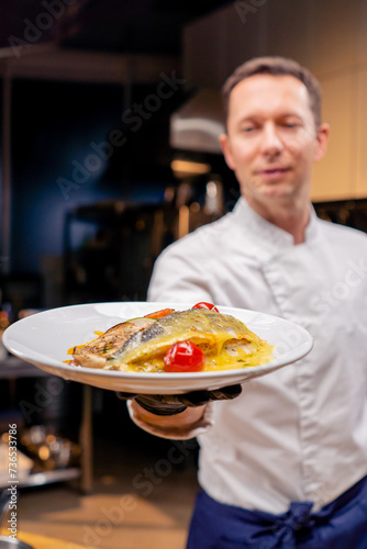 the chef demonstrates a ready-made fish dish at arm's length in professional kitchen