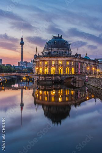 Museum Island in Berlin in the morning. Illuminated buildings and the television tower just before sunrise. Reflections on the water surface from the river Spree and clouds in the sky
