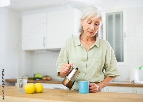 Portrait of smiling mature woman drinking morning coffee at home kitchen