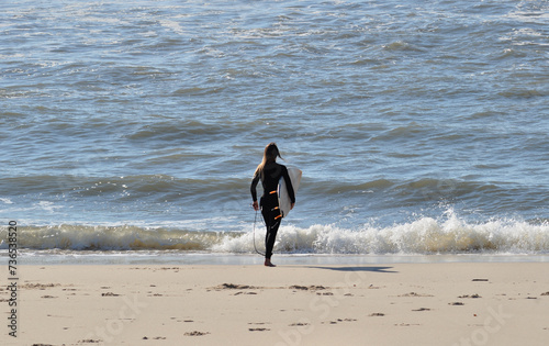 Female surfer with surfboard under her arm entering the sea water to surf