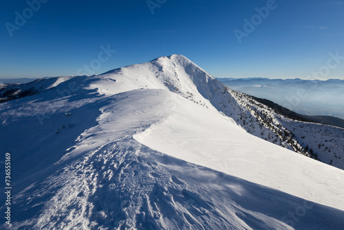 Velky Krivan, Mala Fatra, Slovakia. Beautiful winter landscape of mountains is covered by snow in wintertime. Sunny weather with clear blue sky and blurred flying snow. photo
