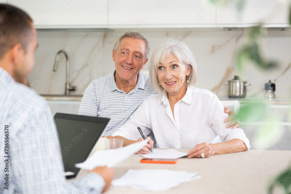 Fototapeta premium Couple of elderly man and woman discussing deal with male salesman in kitchen home