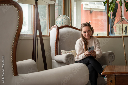 Mujer leyendo desde su teléfono móvil sentada en el sofá de su sala de estar photo