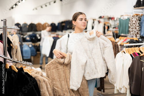 Young woman buyer chooses fur coat in clothing store..