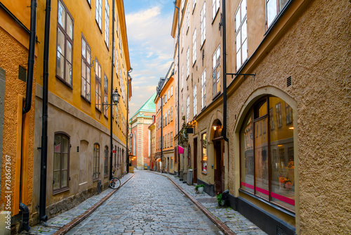A narrow cobblestone alley of shops and cafes with Saint Gertrude German Church in view in the medieval old town of Gamla Stan island in Stockholm  Sweden.