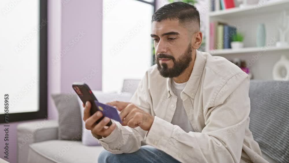 A bearded man using a smartphone comfortably in a modern living room, showcasing technology use in a casual, domestic setting. A bearded man using a smartphone comfortably in a modern living room, showcasing technology use in a casual, domestic setting.