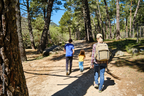 Back view of happy family with backpacks walking in forest