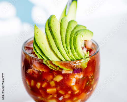 Mexican style seafood cocktail with shrimp, octopus, squid, tomato, tomato sauce and sauces, avocado, inside a seafood restaurant.