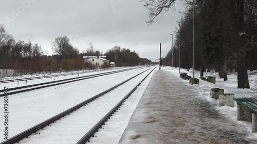 Liepa, Latvia - february 13, 2024- a desolate train platform in winter with multiple tracks, bare trees, and benches covered with snow. photo