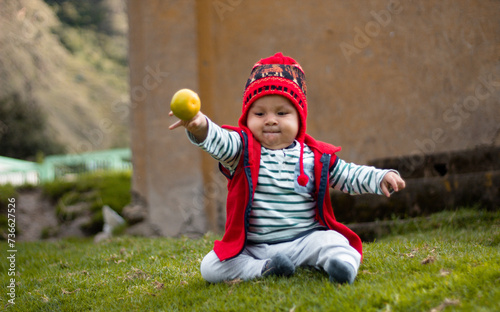 Un bebé sonriente con su chullo tejido, disfrutando del sabor de la naranja, pequeño tesoro andino, estilo de vida saludable, quechua, al aire libre