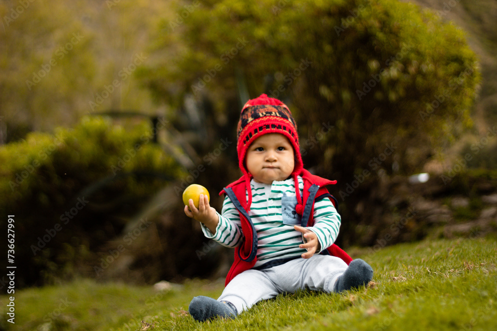 Un bebé sonriente con su chullo tejido, disfrutando del sabor de la naranja, pequeño tesoro andino, estilo de vida saludable, quechua, al aire libre Un bebé sonriente con su chullo tejido, disfrutando del sabor de la naranja, pequeño tesoro andino, estilo de vida saludable, quechua, al aire libre