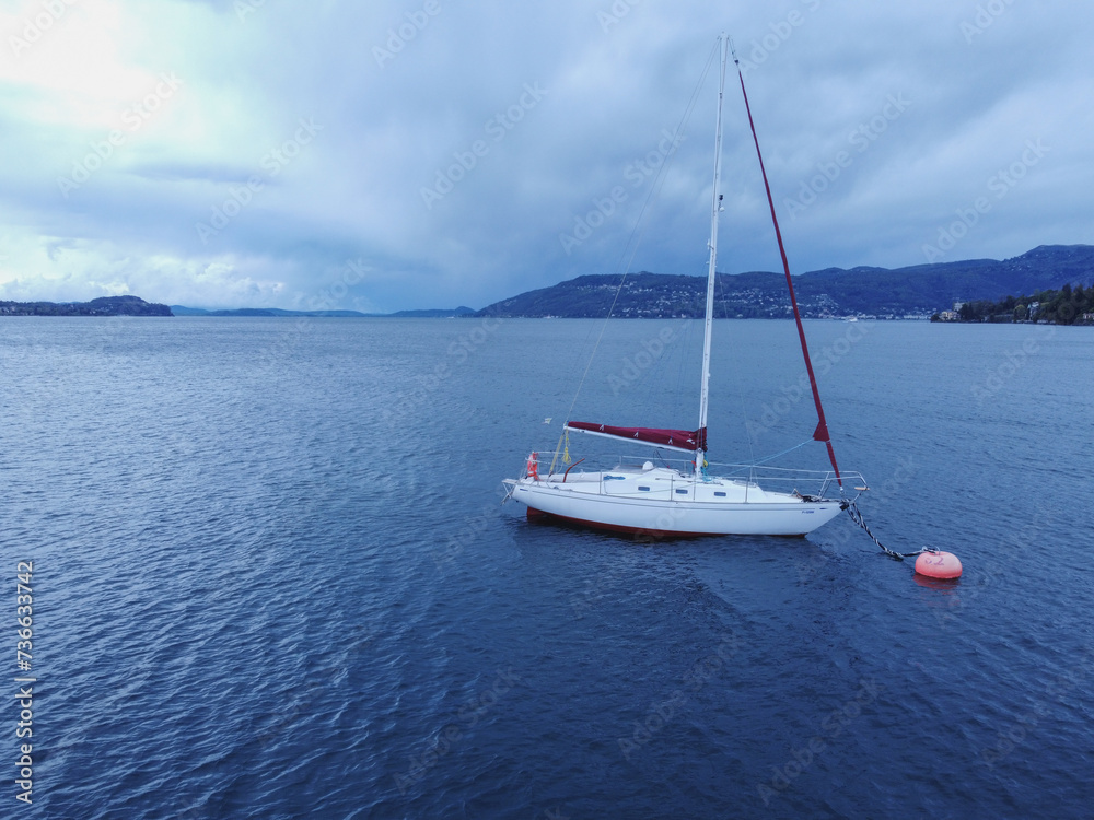 Fototapeta premium Sailboat in the sea in the evening sunlight over beautiful big mountains 