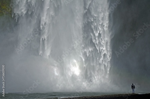 Man in front of falling masses of water of a waterfall, Skogafoss, Iceland, Europe photo