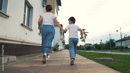 Happy family mother and son running at suburb street holding hands having fun together back view. Cheerful woman mom and little male kid child playing rejoice speed movement outdoor leisure activity
