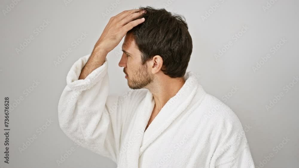 Handsome young man in white robe touches his hair and beard against a plain background Handsome young man in white robe touches his hair and beard against a plain background