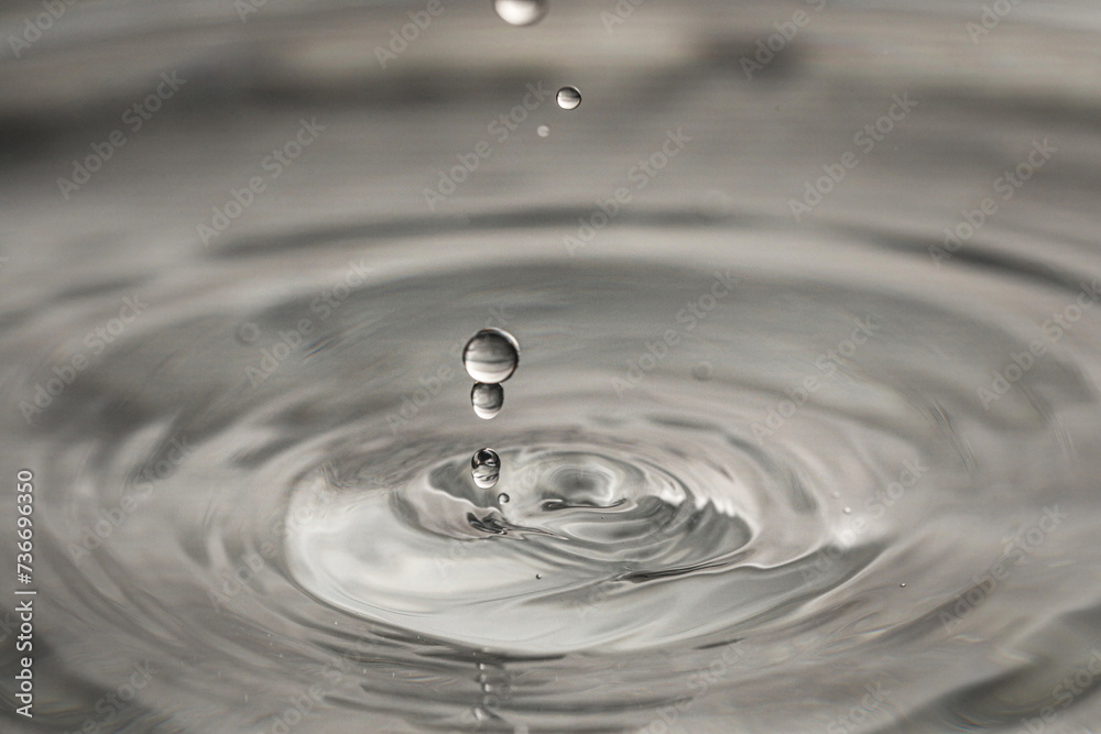 Drops falling into clear water on grey background, closeup Drops falling into clear water on grey background, closeup
