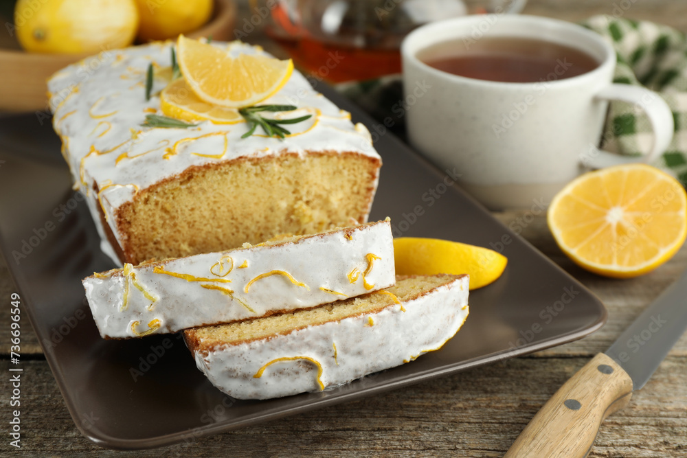Tasty lemon cake with glaze and tea on wooden table, closeup