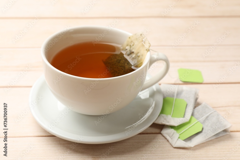 Tea bags and cup of hot beverage on light wooden table, closeup Tea bags and cup of hot beverage on light wooden table, closeup