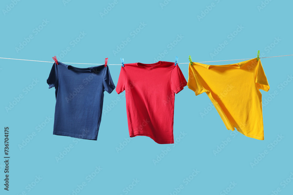 Colorful t-shirts drying on washing line against light blue background